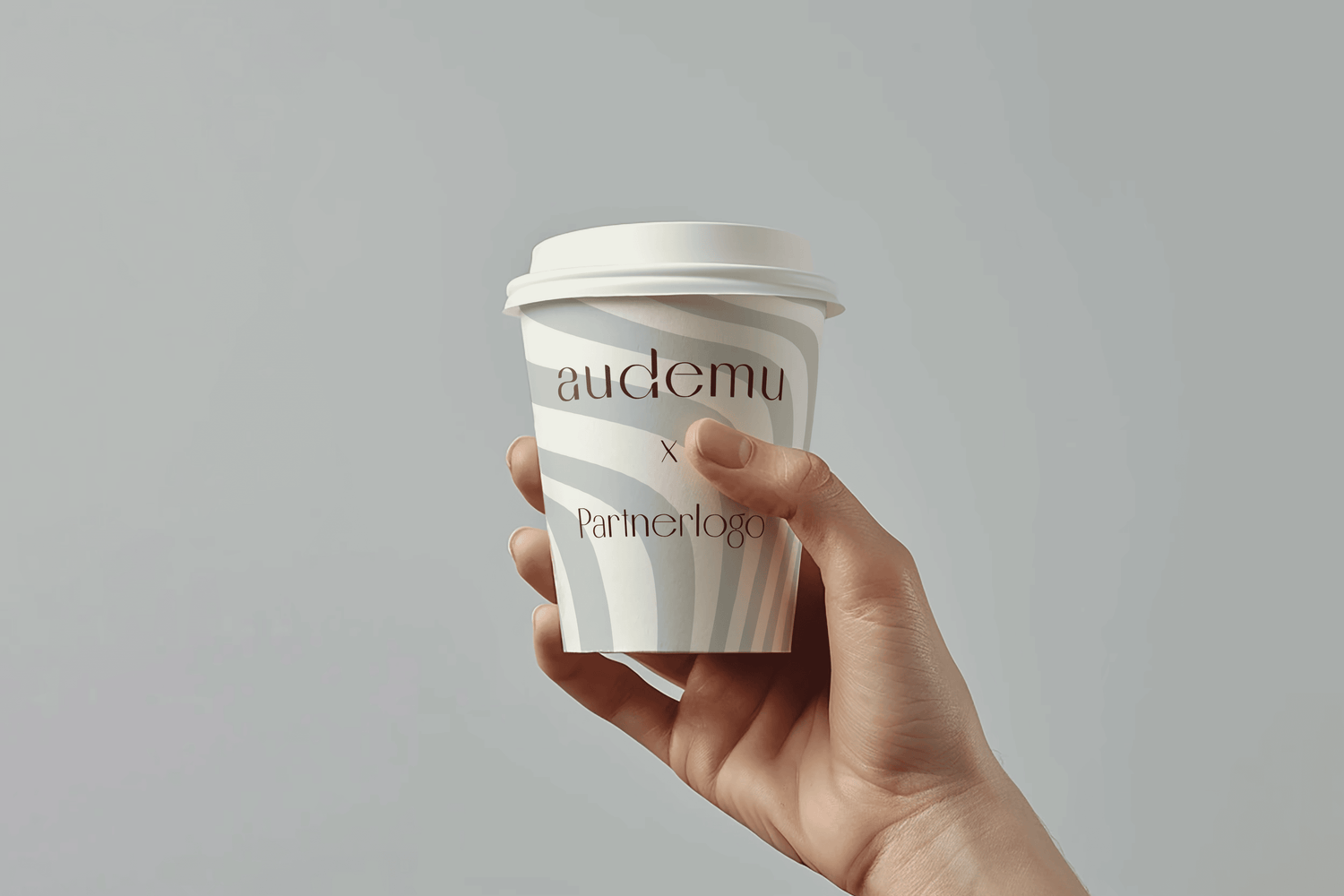 Hand hält eine weiße Papptasse mit dem Audemu-Logo und dem Schriftzug „Partnerlogo“ – diagonale Streifen im Design symbolisieren die B2B-Kollaboration. Hintergrund in neutralen Grautönen betont die Markenpräsenz.