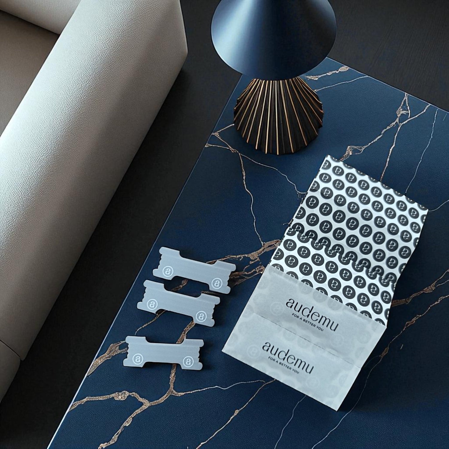 Audemu Nasenstrips oder auch The Nasal Strip in minimalistischer Präsentation auf einem dunkelblauen Marmor-Tisch neben einer modernen Lampe und einer eleganten Verpackung mit dem Markenslogan „For a Better You“.