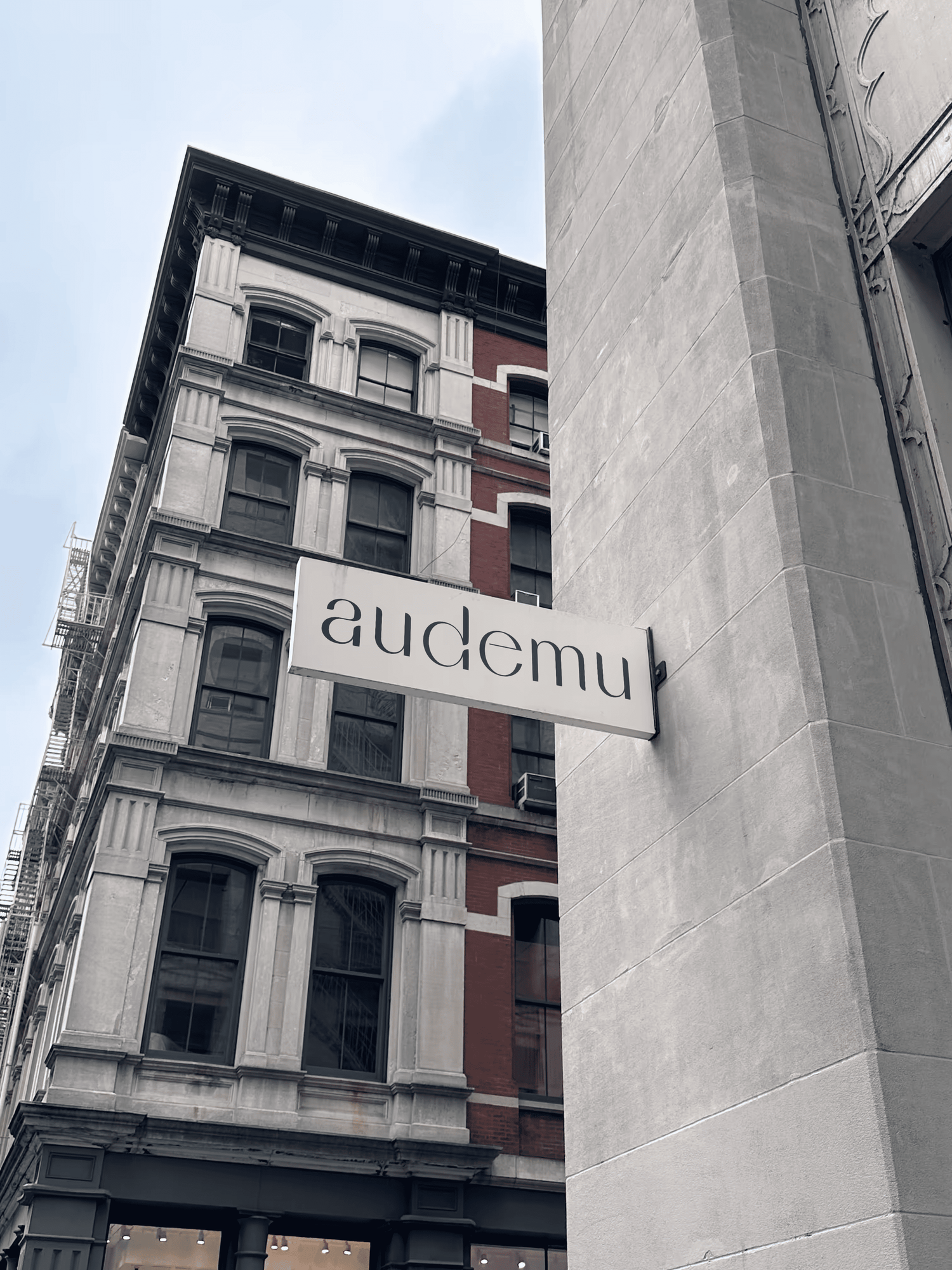 Audemu-Geschäftsschild an einem historischen Gebäude – schwarz-weißes Design mit dem Markennamen „audemu“ in moderner Schrift. Das Schild ist auf einer Fassade befestigt, die klassische Architekturelemente wie Fenster und Dekorationen zeigt.
